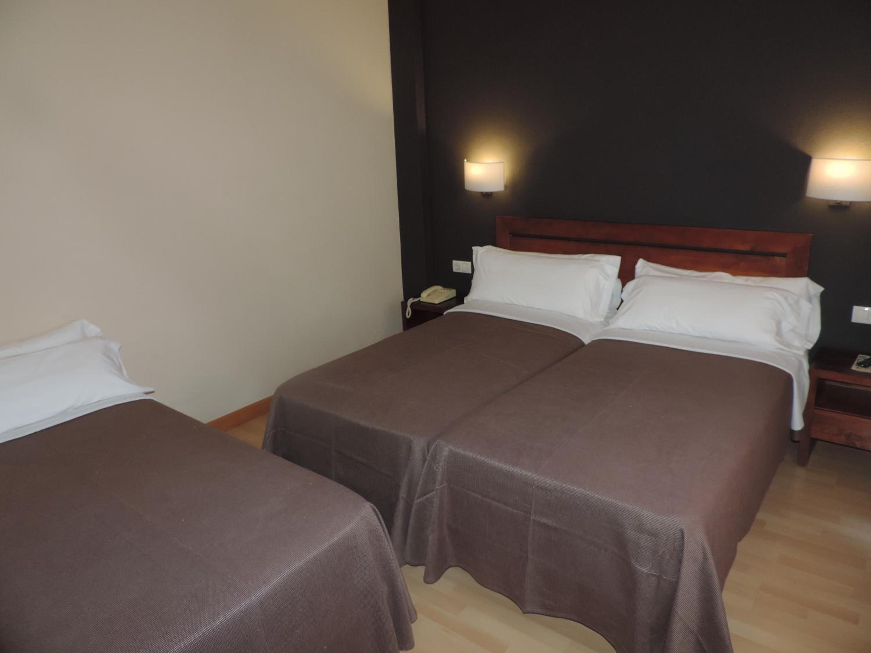 Habitación de hotel con dos camas, un cabecero de madera, lámparas de noche y una mesita de noche con un teléfono.