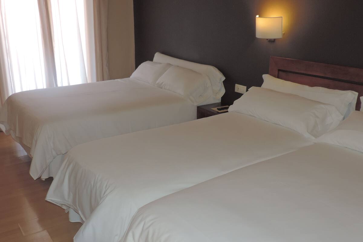 A hotel room with two beds, a nightstand, and a wall-mounted lamp.