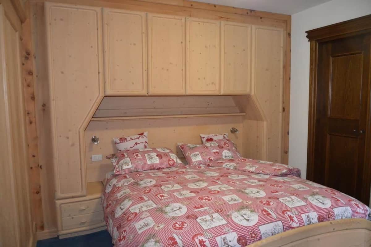 A bedroom with a wooden headboard, a bed with a red and white checkered bedspread, and a wooden wardrobe.