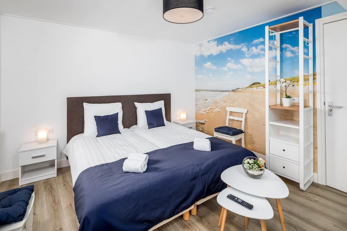 Hotellihuone, jossa on sänky, yöpöydät, pieni pöytä, jossa on kulho täynnä hedelmiä, tuoli ja vaatekaappi.