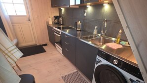 A compact kitchen with a washing machine, a sink, and a coffee maker. - Café de Upernavik (Upernavik)