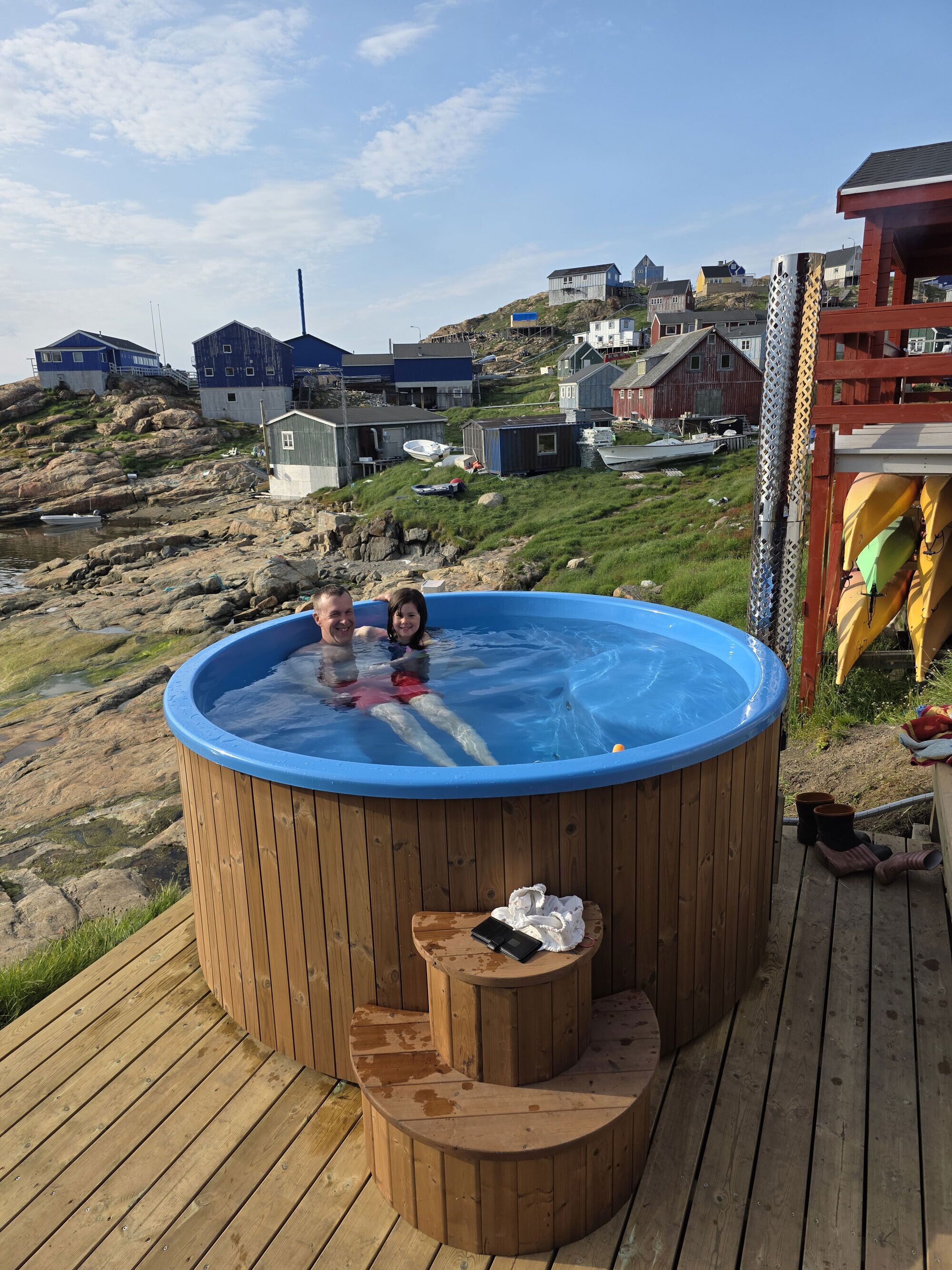 Een houten jacuzzi op een terras met uitzicht op huizen op een heuvel.