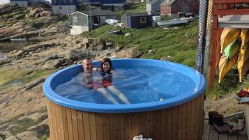 Een houten jacuzzi op een terras met uitzicht op huizen op een heuvel.