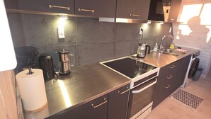 A modern kitchen with dark cabinets, stainless steel countertops, a built-in oven, and a microwave. - Café de Upernavik (Upernavik)