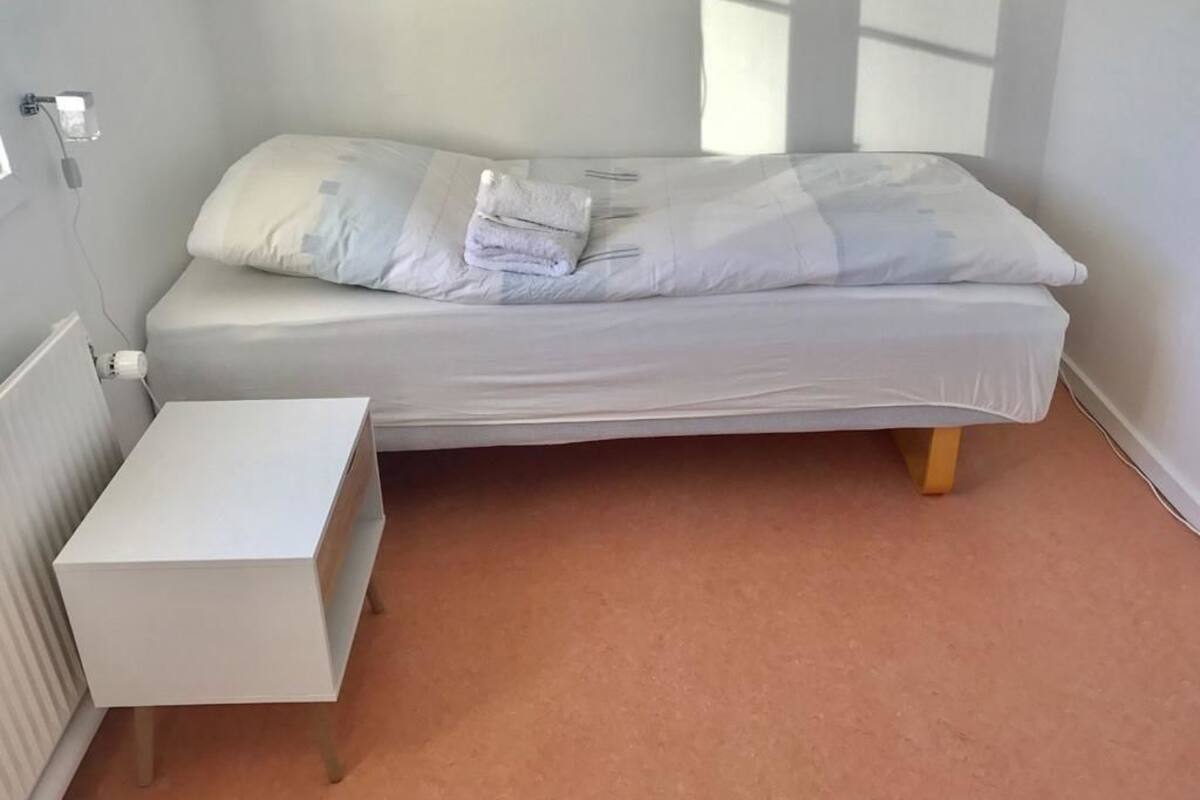 Une petite chambre à coucher, bien rangée, avec un lit simple, une table de chevet et un radiateur.