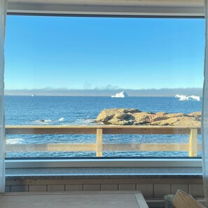 A view of the ocean through a window with a wooden railing. - Café de Upernavik (Upernavik)