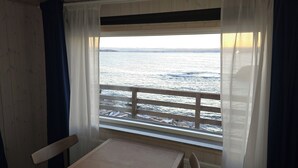 A room with a wooden table and chairs, a window with a view of the sea, and a wooden ceiling. - Café de Upernavik (Upernavik)