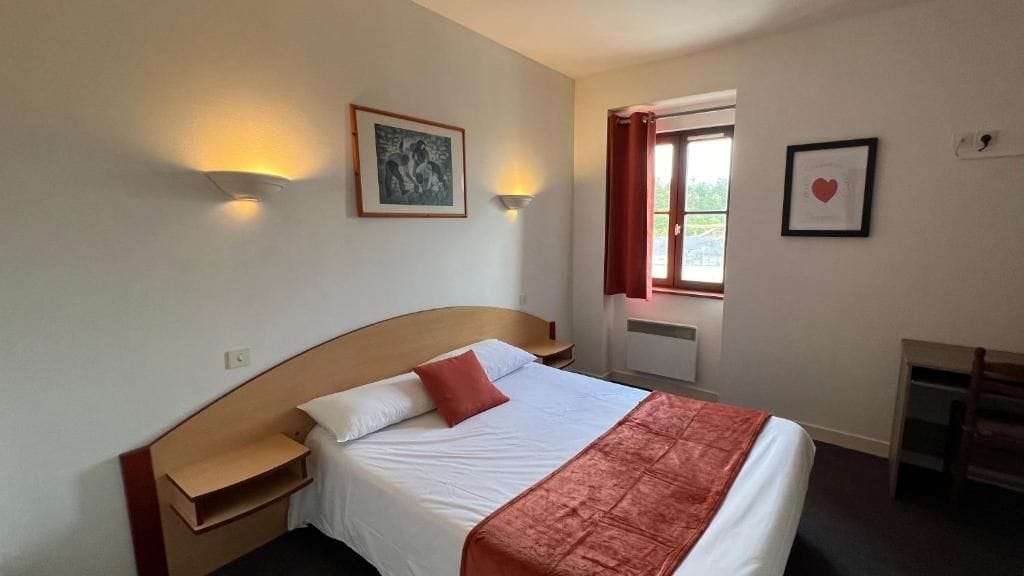 Une chambre d’hôtel avec un lit, des tables de chevet, un bureau et une fenêtre avec des rideaux.