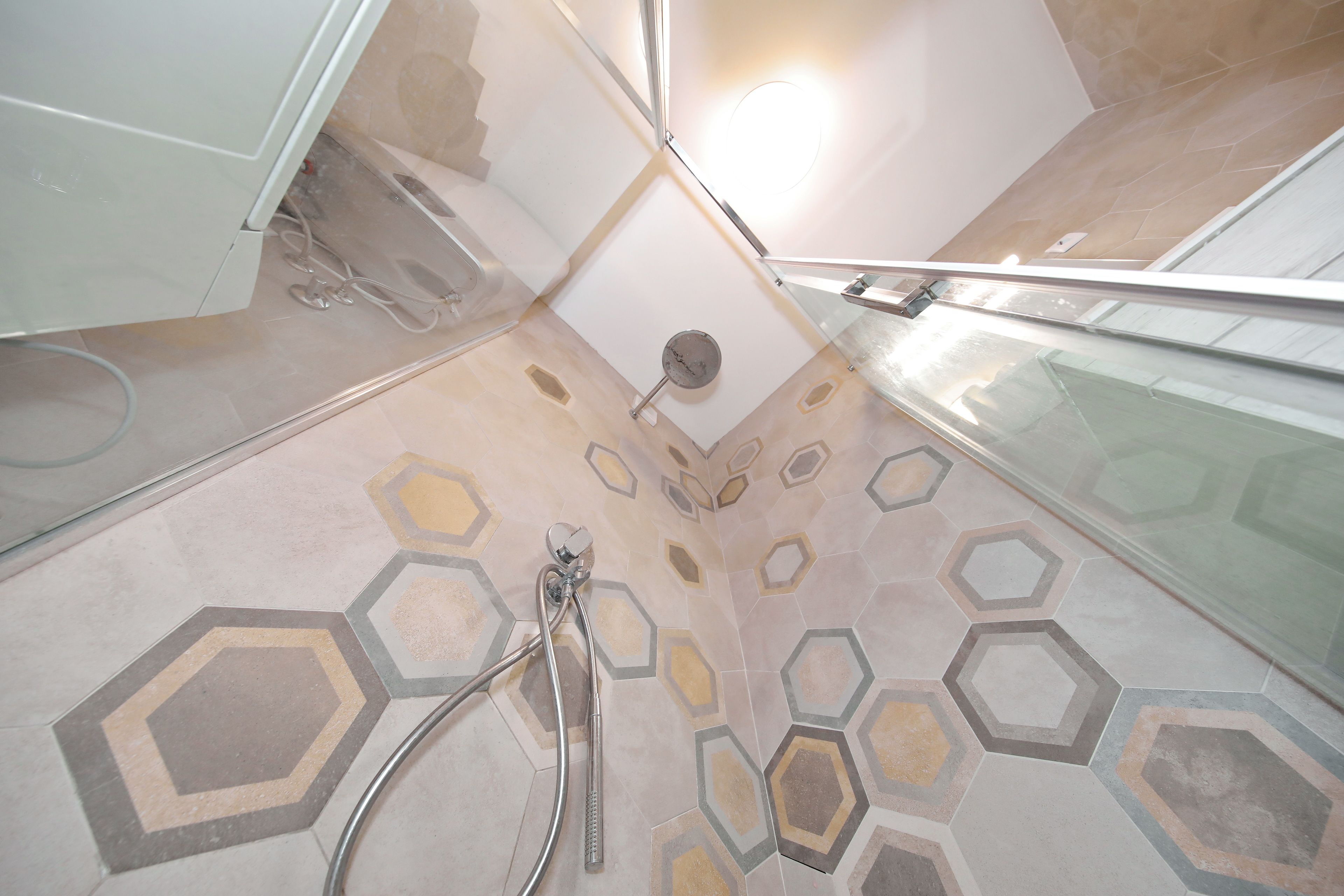 Un espace douche avec un motif de carrelage hexagonal et une cabine de douche fermée par des parois en verre.