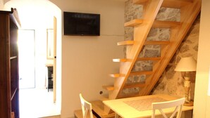 A small dining area with a wooden table and chairs, a staircase with a wooden railing, and a television mounted on the wall. - Stone House Apartment (Preko)