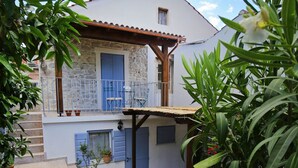 A two-story building with a balcony, potted plants, and a dirt ground. - Stone House Apartment (Preko)