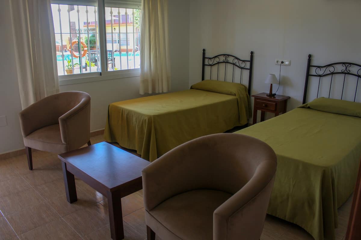 Una habitación con dos camas, una silla, una mesita y una ventana con cortinas.