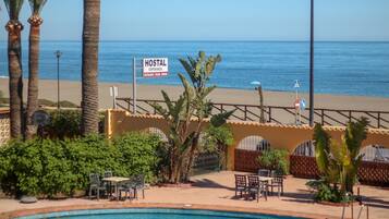 A pool area with a sign indicating a hostel, palm trees, and a view of the beach.
