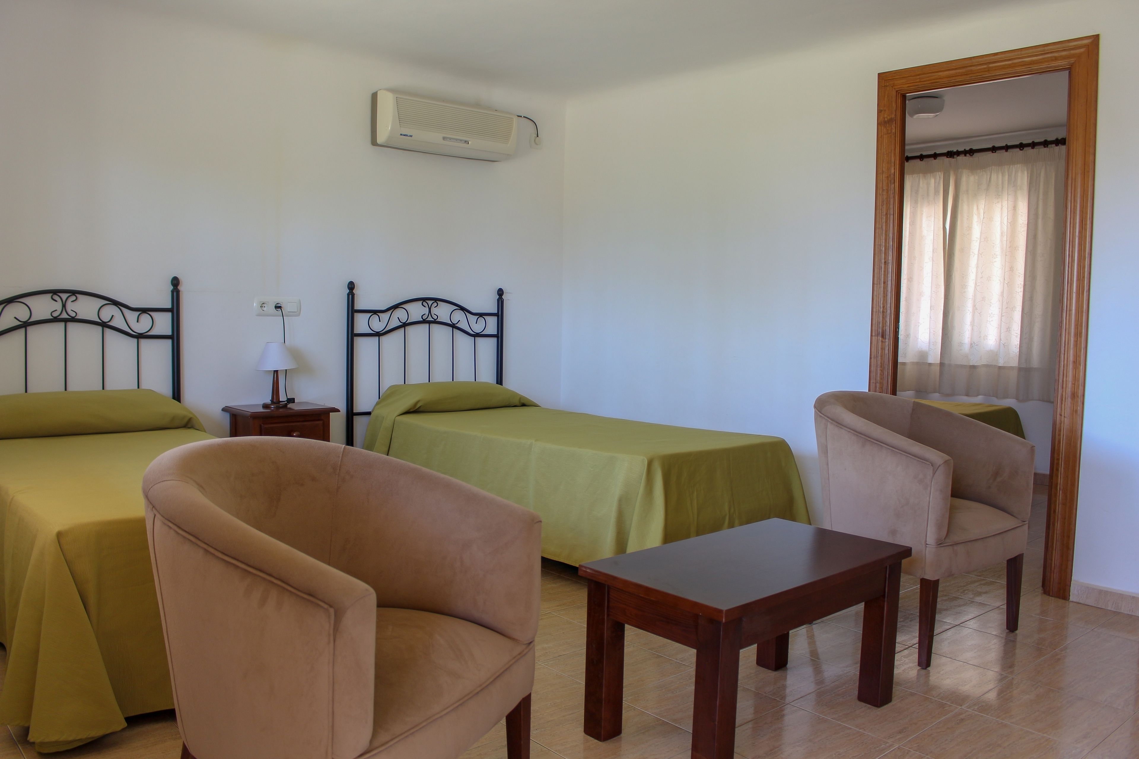 A room with two beds, a chair, a table, and an air conditioning unit.