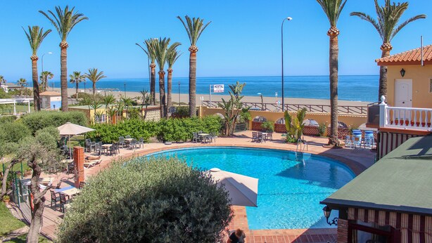 A pool area with palm trees, lounge chairs, and a sign indicating a hostel. - Hostal Esperanza (Velez-Malaga)