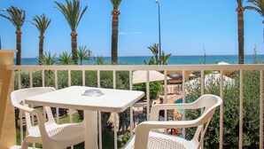 A balcony with white plastic chairs and a table, overlooking a pool area with palm trees and a clear blue sky. - Hostal Esperanza (Velez-Malaga)