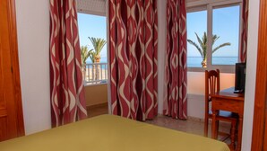 A hotel room with a bed, a desk, and a view of the beach. - Hostal Esperanza (Velez-Malaga)