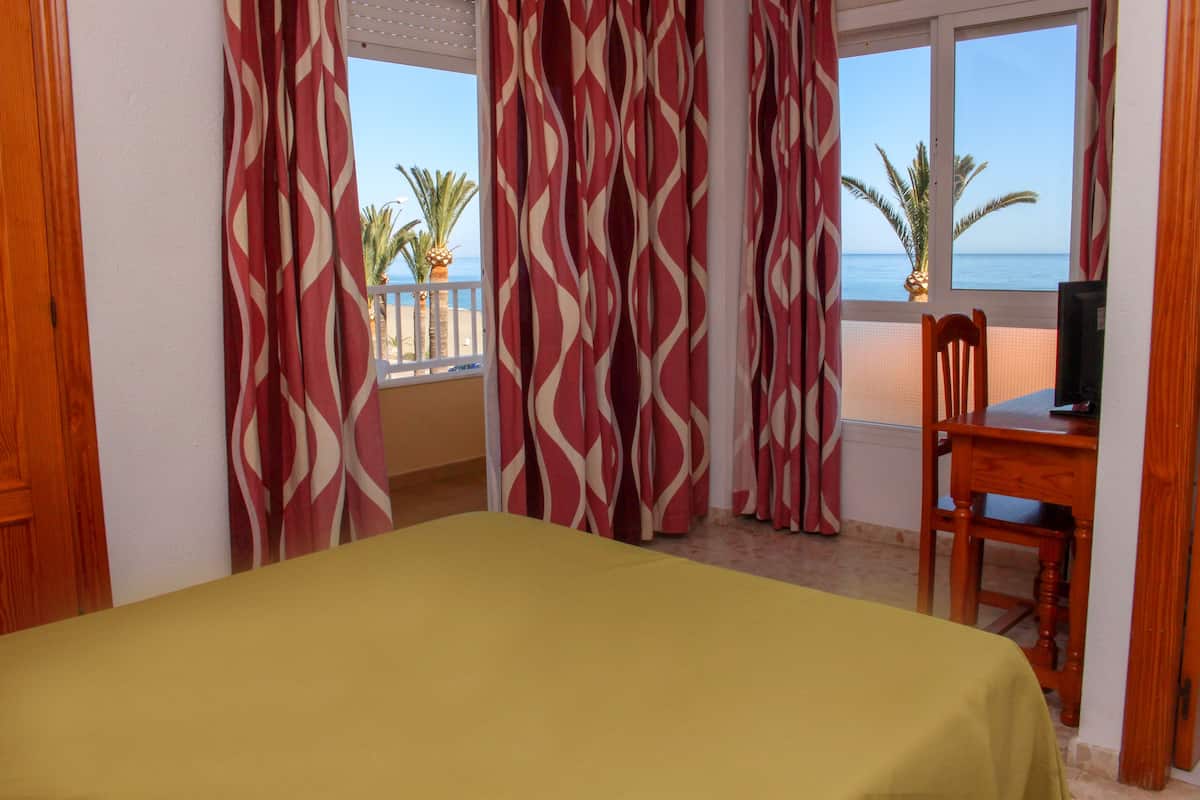 Una habitación de hotel con cama, escritorio y vista a la playa.
