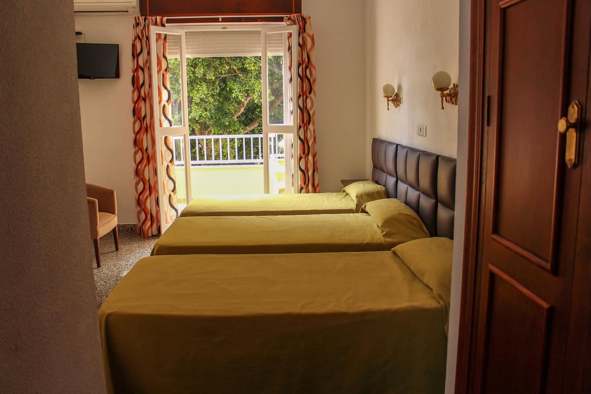 Habitación de hotel con dos camas, un televisor en la pared y un balcón con cortinas.
