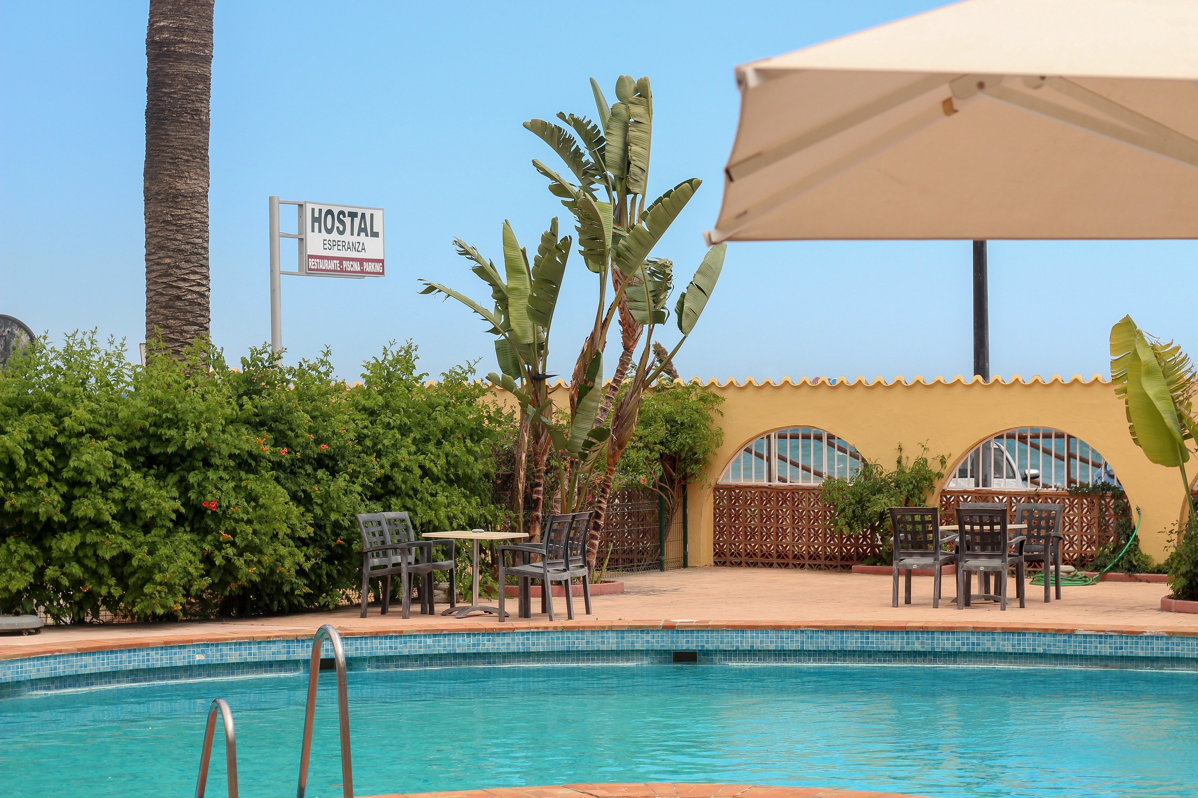 Un espace piscine agrémenté d’un panneau indiquant « HOSTAL ESPERANZA », ainsi qu’un restaurant, un parking et un espace de repos couvert.