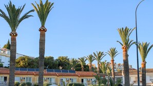 A building with a red-tiled roof, palm trees, and a street lamp. - Hostal Esperanza (Velez-Malaga)