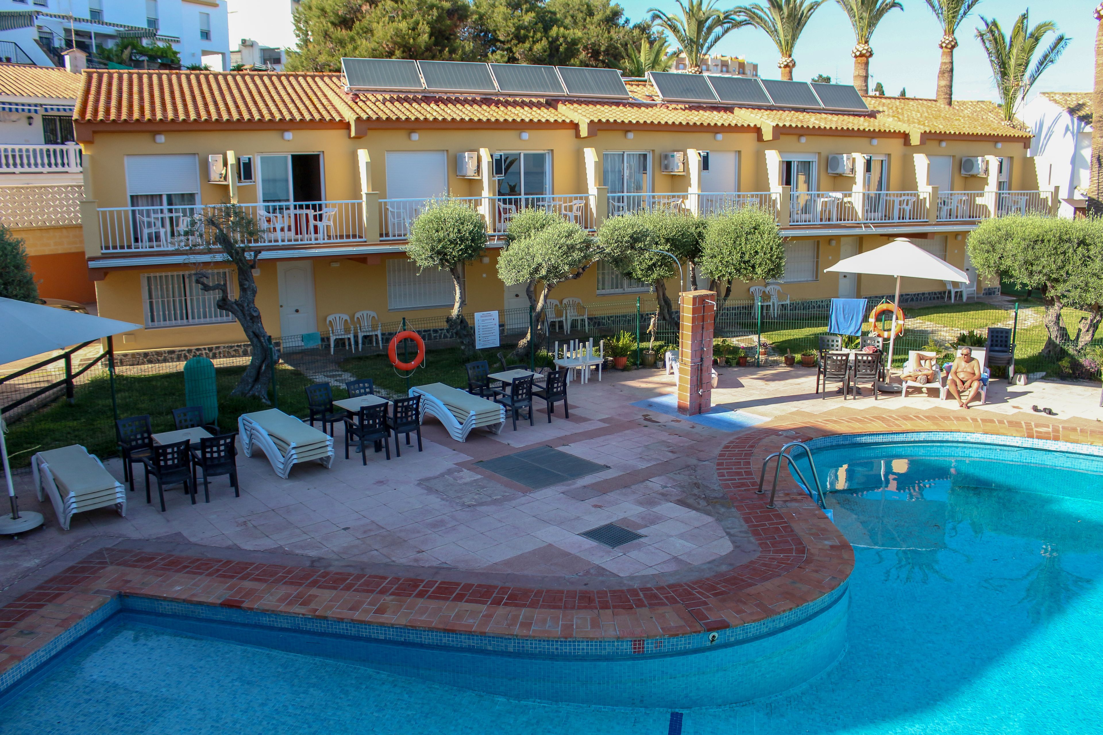 A hotel with a swimming pool, outdoor seating, and solar panels on the roof.