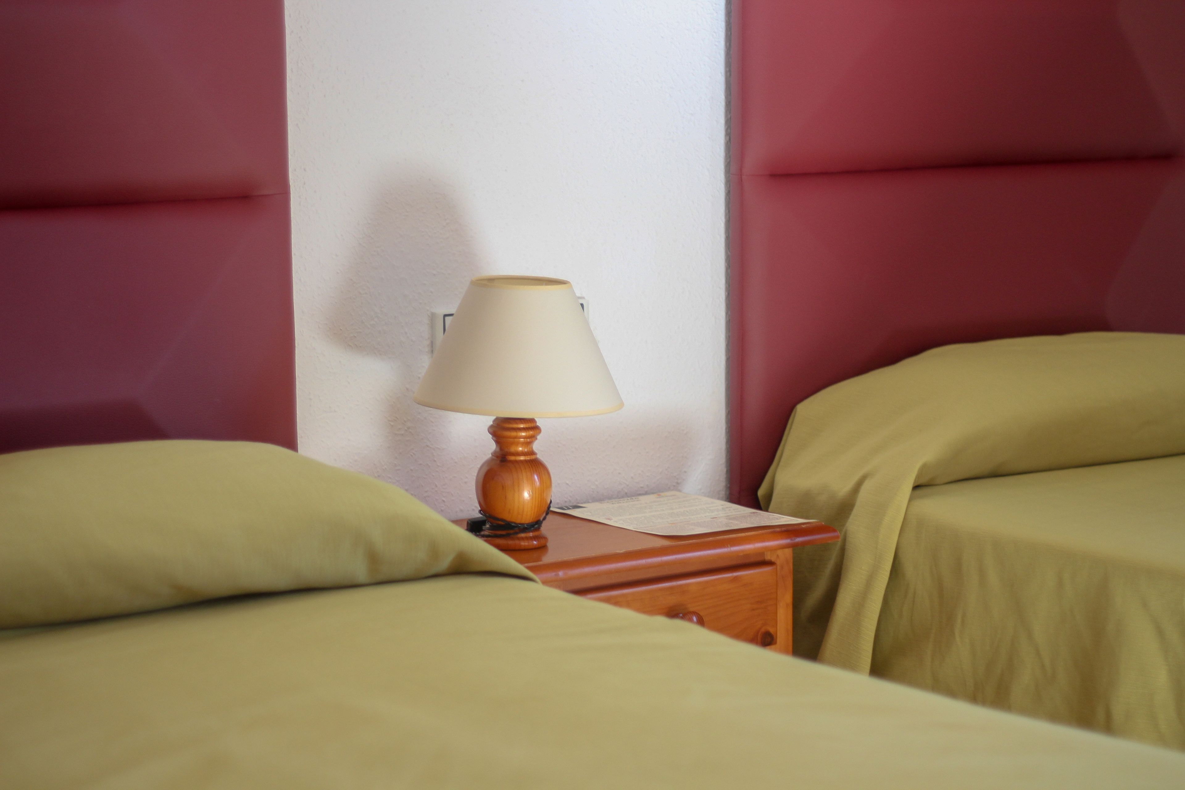 Una habitación con dos camas, una mesita de noche de madera con una lámpara y una pared con un diseño texturizado.
