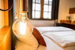 A room with a bed, a hanging light fixture, and a window with curtains. - Zur Krone (Grossheubach)