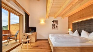 A bedroom with a wooden bed, a desk, and a chair. There is a window providing a view of the outdoors.