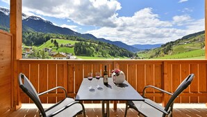 A wooden deck with a table set for two, a bottle of wine, and a vase with flowers.