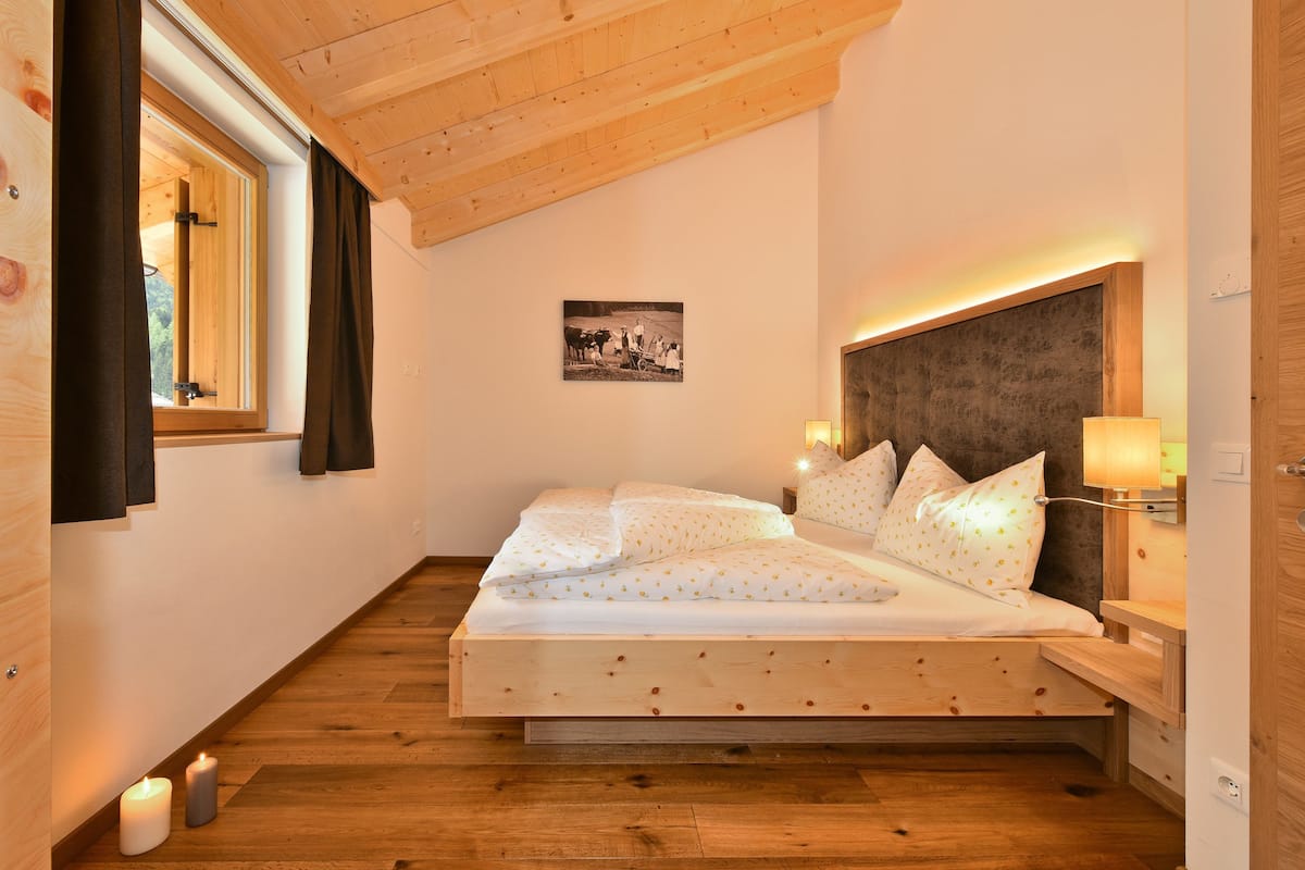 Ein Schlafzimmer mit hölzernem Gestell, einem Bett, Nachttischlampen und einem Bild an der Wand.