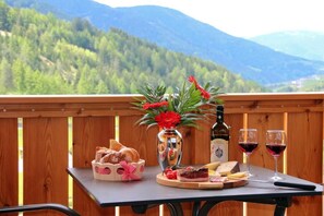 A table with bread, cheese, a bottle, and wine glasses on a balcony with a mountain view. - Proihof (Funes)