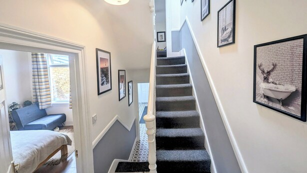 A staircase with a black carpet, white walls, and framed pictures. - TopHome Stoke Newington (London)