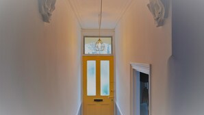 A narrow hallway with a yellow door at the end, a window above the door, and a light fixture hanging from the ceiling. - TopHome Stoke Newington (London)