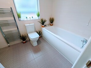 A bathroom with a toilet, a bathtub, a towel rack, and several potted plants. - TopHome Stoke Newington (London)