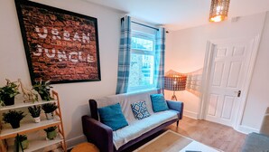 A living room with a sofa, a coffee table, a rug, a bookshelf, and a window with curtains. - TopHome Stoke Newington (London)