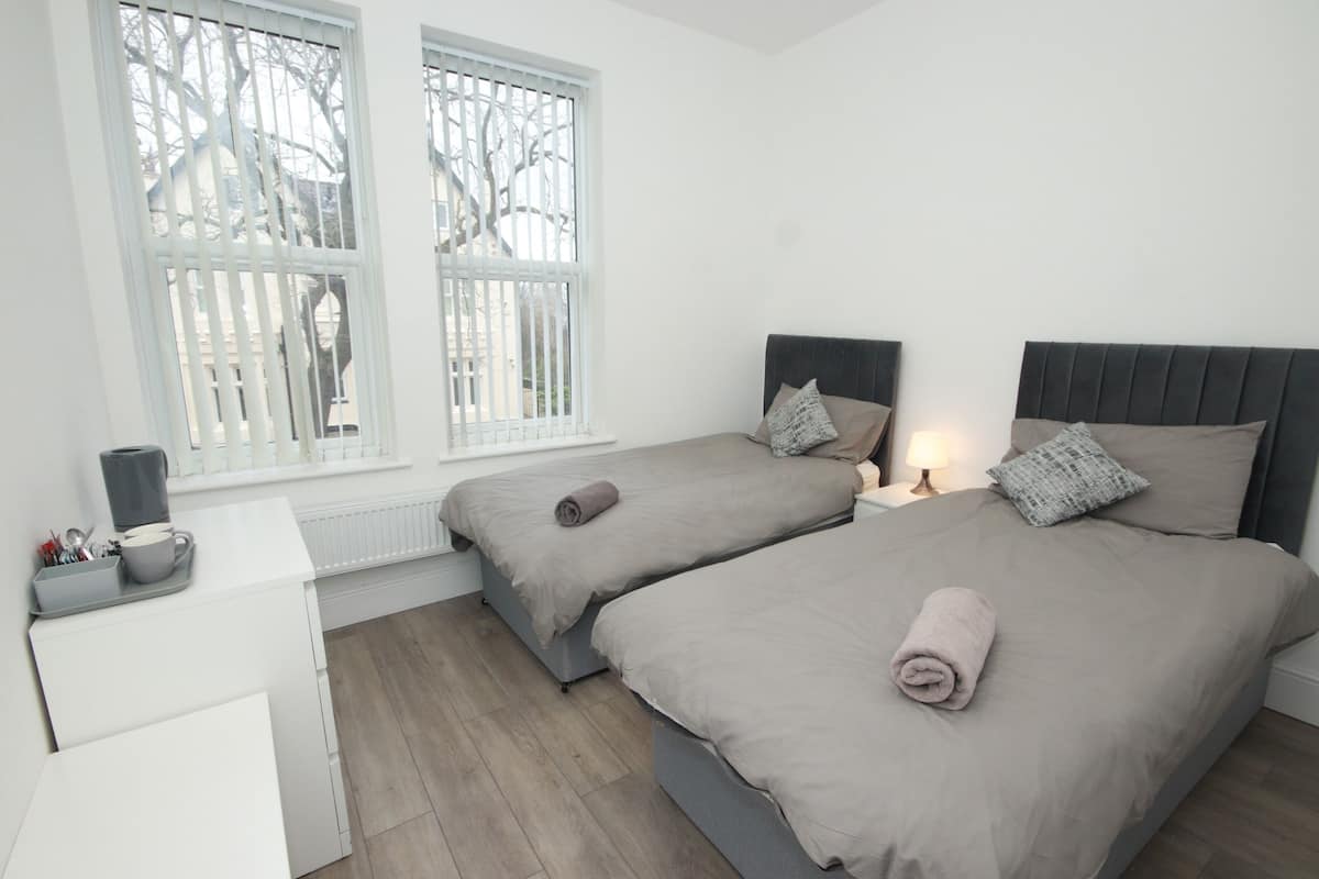 Une chambre avec deux lits, un petit bureau et une fenêtre avec des stores.
