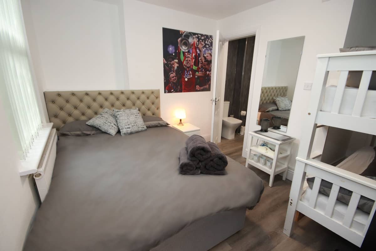 Une chambre à coucher avec un grand lit, une table de chevet, une commode, un miroir et une porte donnant sur une autre pièce.