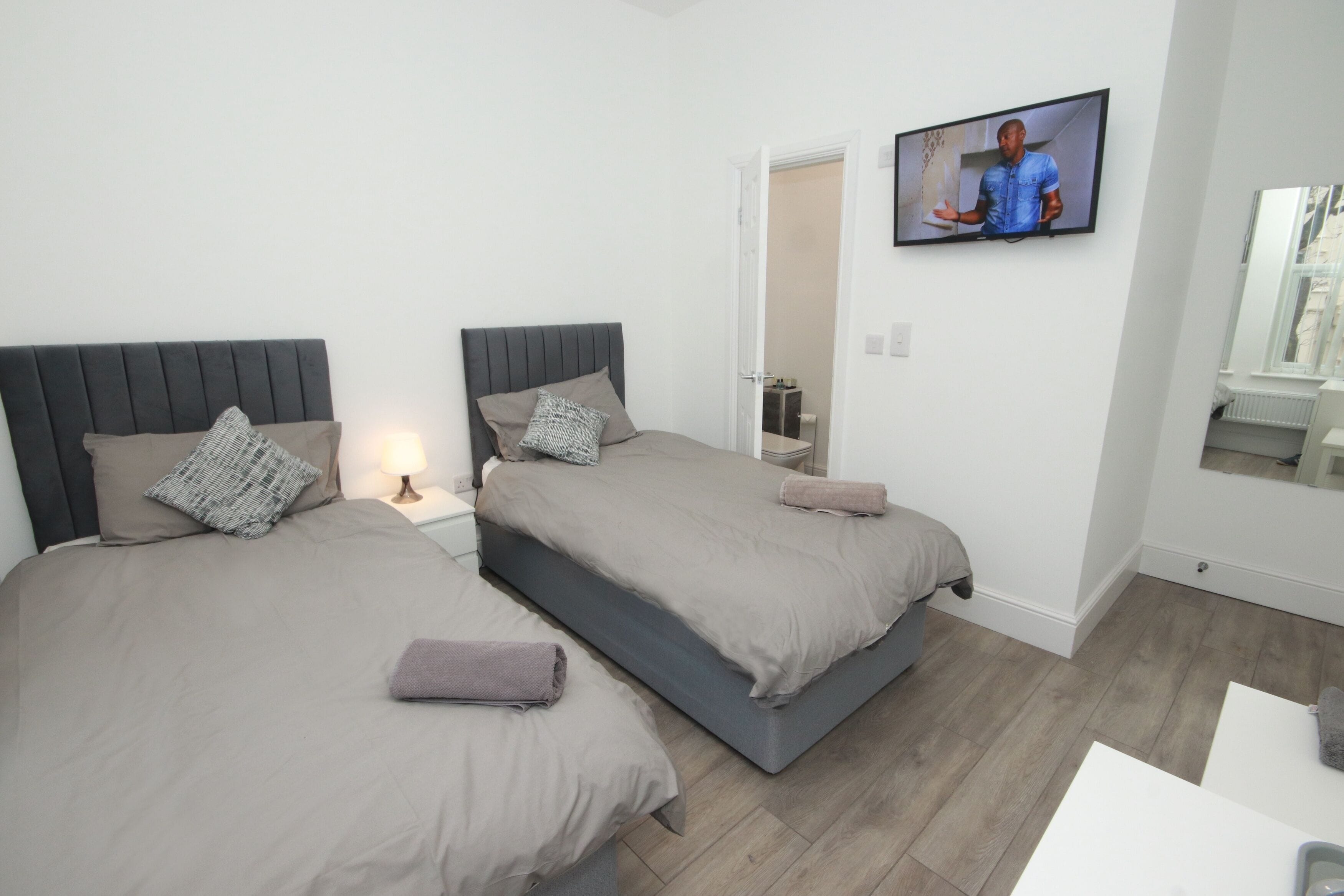 A hotel room with two beds, a TV mounted on the wall, a small table, and a mirror.