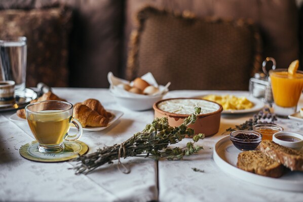 A breakfast setting with croissants, a cup of tea, a bowl of cheese, and a glass of orange juice on a table.
