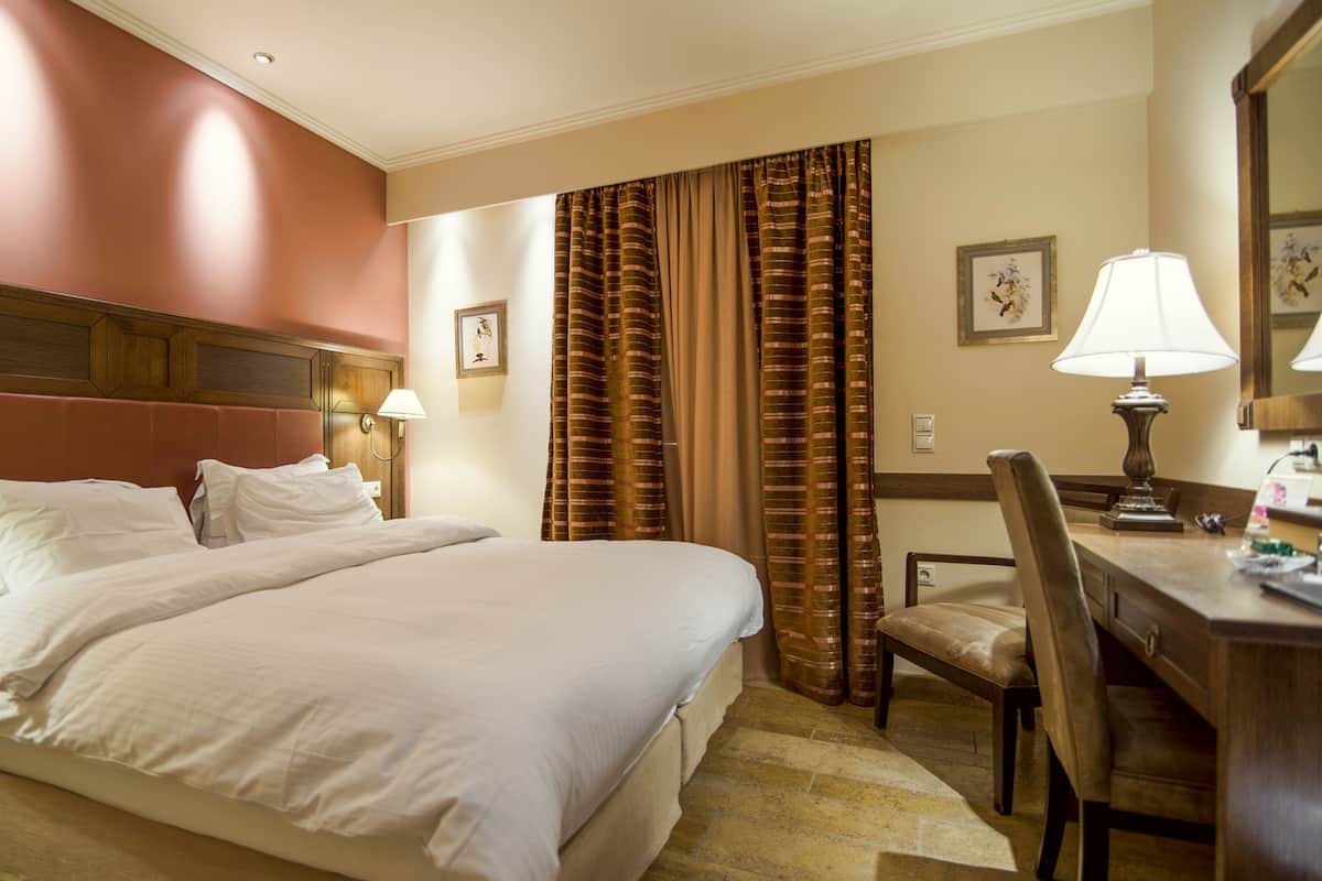 Una habitació d'hotel amb un llit gran, una taula de treball amb una cadira, una làmpada i cortines.