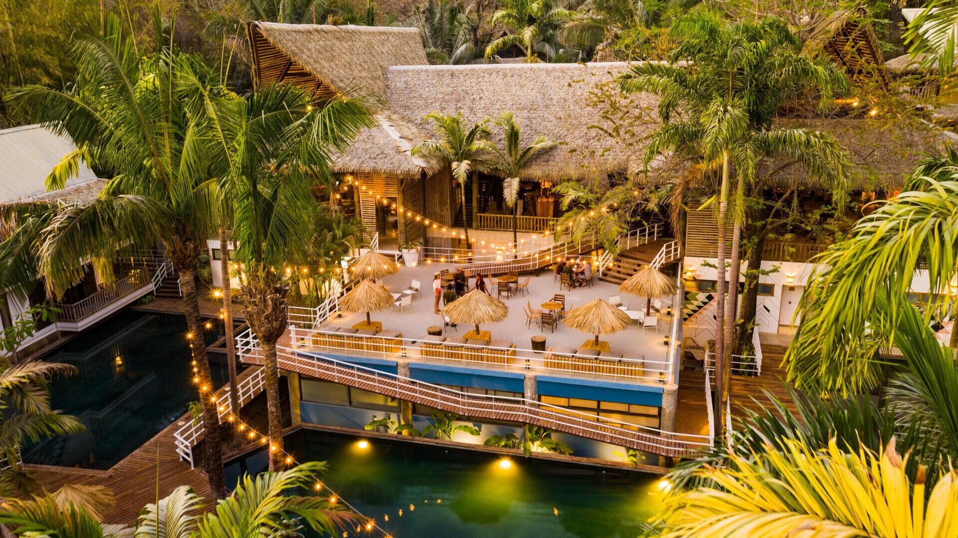 Un resort con piscina, construcciones de techo de paja y zonas de estar al aire libre rodeadas de palmeras.