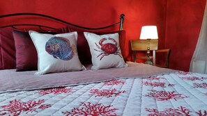 A bed with two decorative pillows, a bedside table with a lamp, and a red wall. - Agriturismo Gocce di Luna (Celle Ligure)