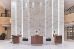 Un área de recepción con columnas de mármol, barandilla de vidrio y diseño moderno.