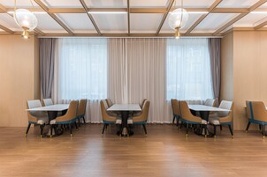 Un comedor amplio con una larga mesa y múltiples sillas, ventanas grandes con cortinas translúcidas e iluminación colgante moderna.
