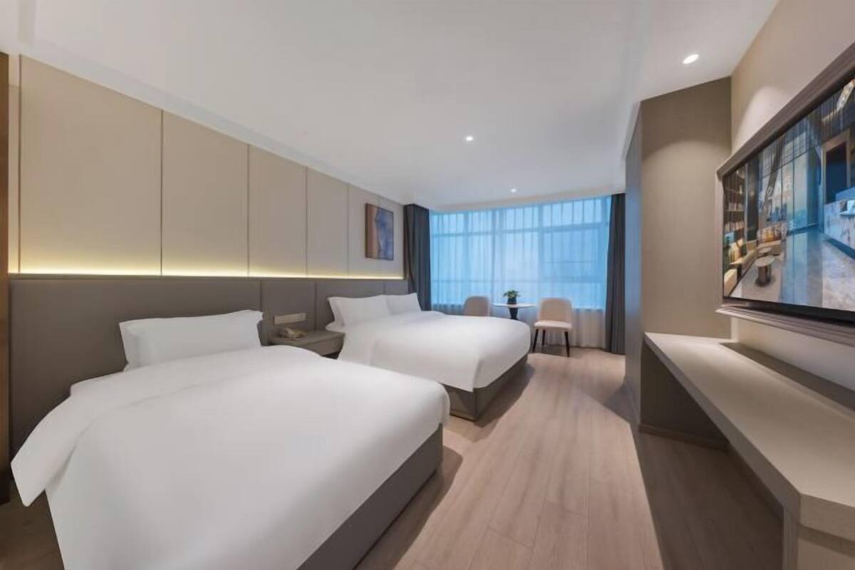 Ein Hotelzimmer mit zwei Betten, einem Fernseher, einem Schreibtisch und einem großen Fenster.