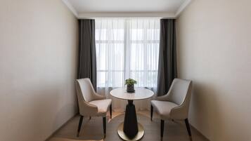 A hotel room with a round table, two chairs, a potted plant, and a large window with curtains.