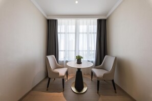 Ein Hotelzimmer mit einem runden Tisch, zwei Stühlen, einem Blumentopf und einem großen Fenster mit Vorhängen.