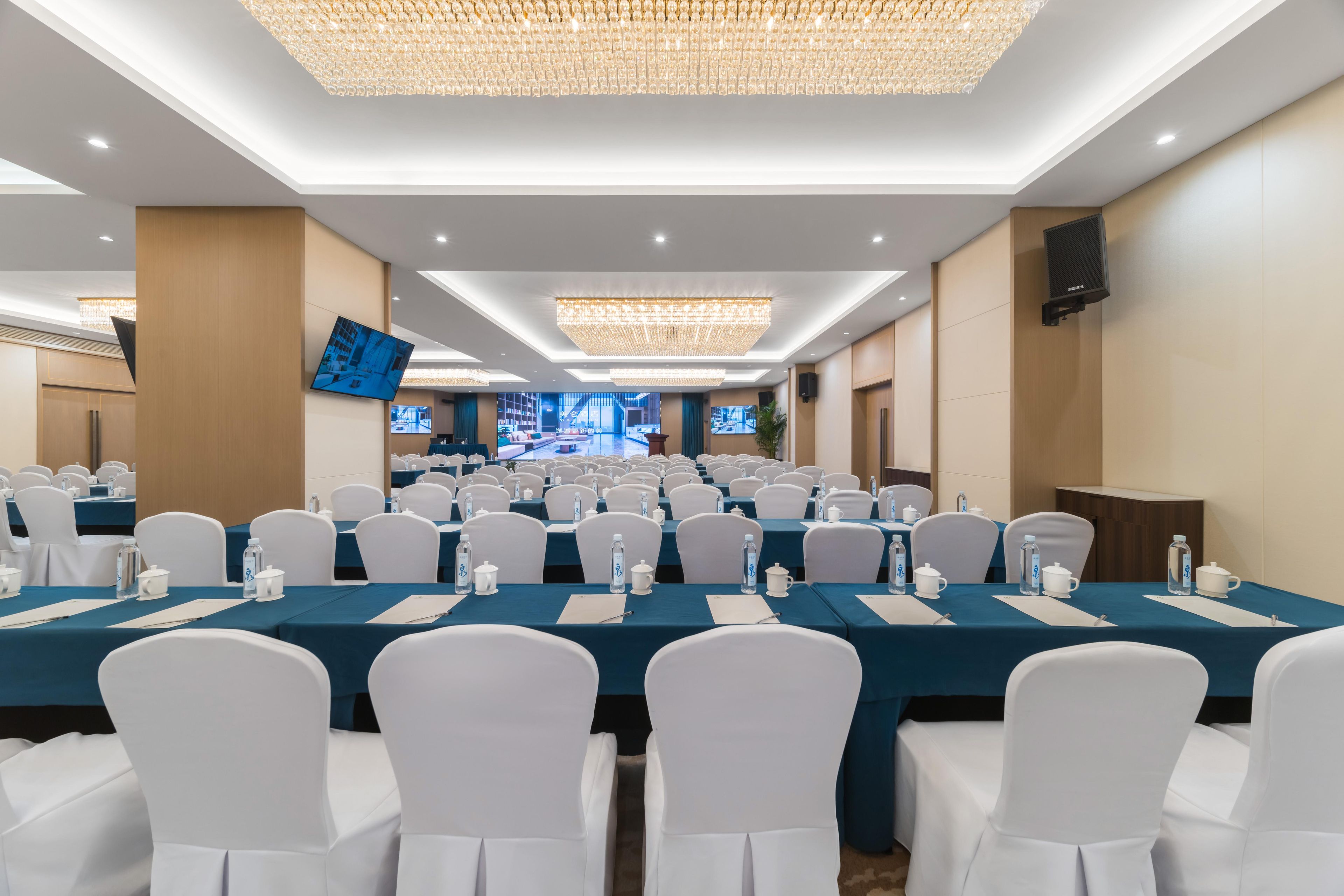 A conference room with rows of tables, white chairs, and a large screen.