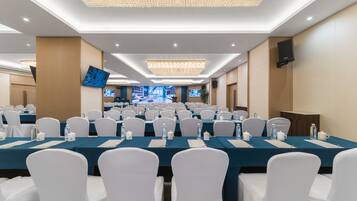 A conference room with rows of tables, white chairs, and a large screen.